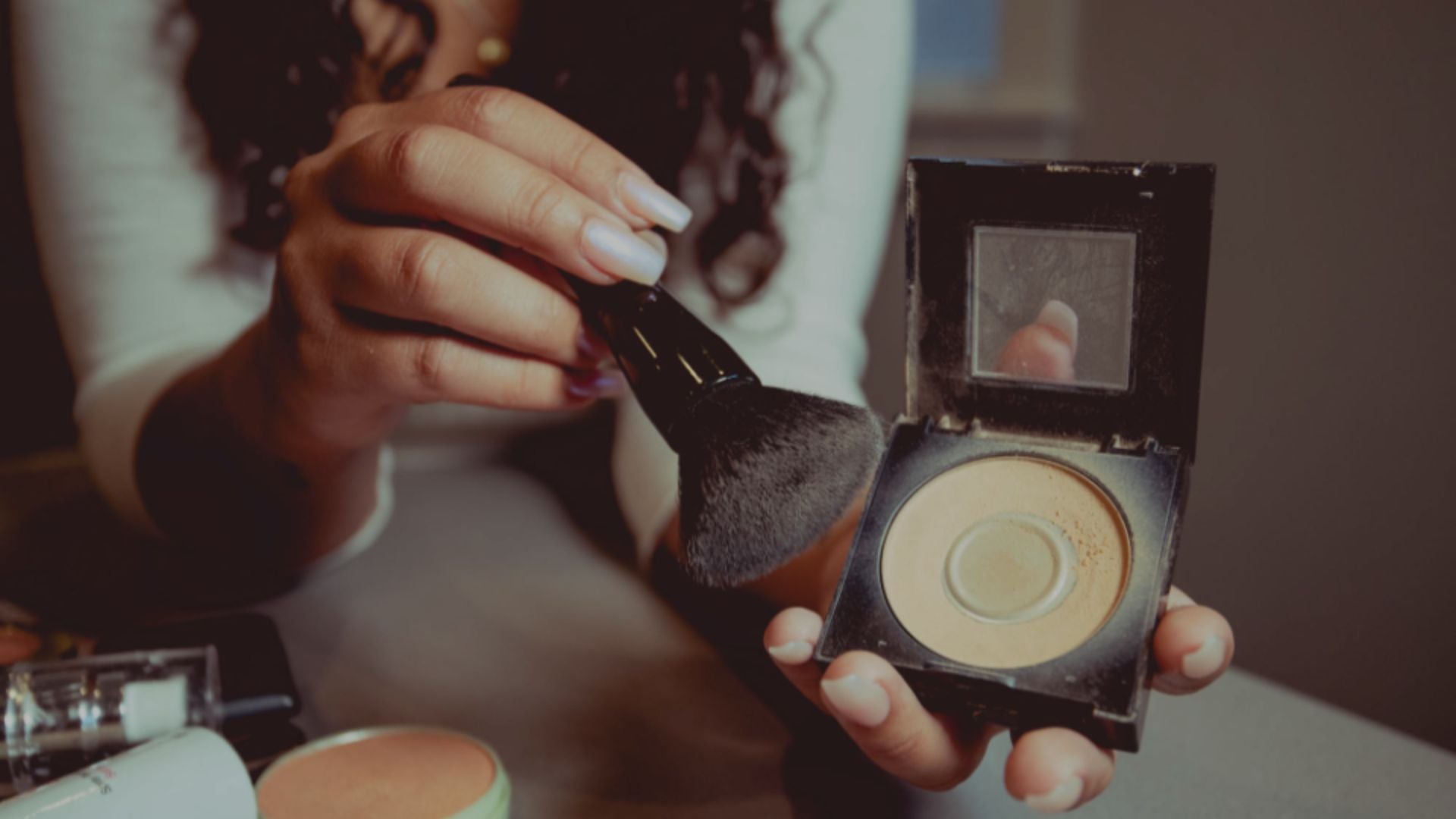 Person holding a makeup brush and compact powder with a blurred background